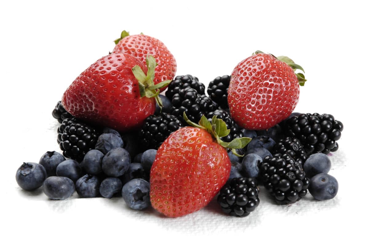 Pile of fresh strawberries, blackberries, and blueberries on a white background.