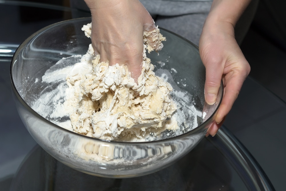 Close-up of hands kneading dough in a glass bowl.