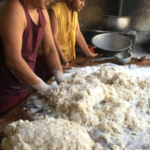 Two men vigorously kneading dough in a rustic setting.