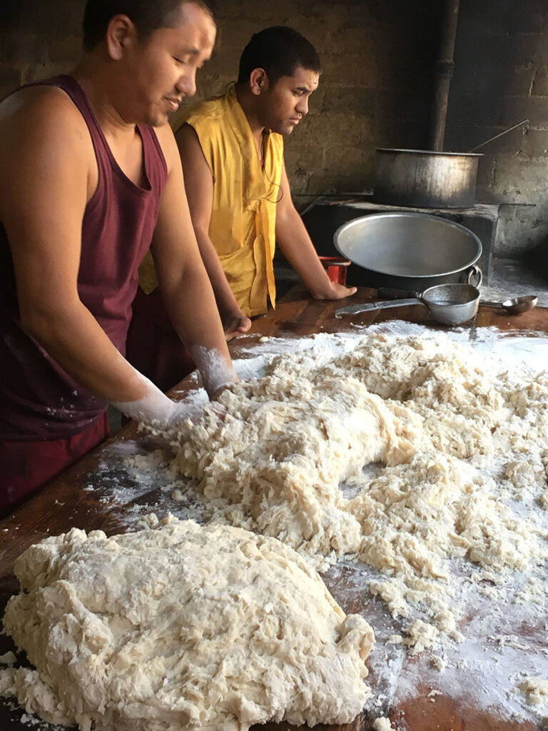 Two men vigorously kneading dough in a rustic setting.