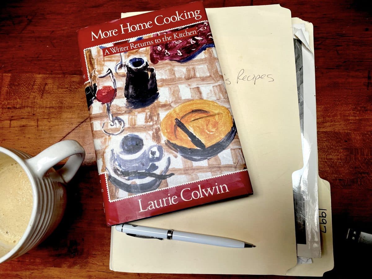 Cover of "More Home Cooking" book by Laurie Colwin on a table next to a mug and pen.