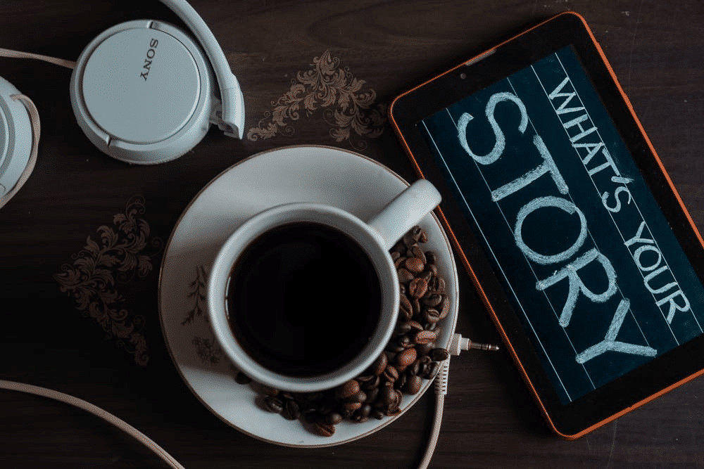 A cup of coffee, headphones, and a tablet displaying the word "Story".