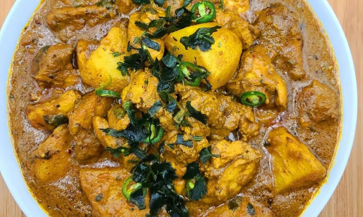 A rich chicken and potato curry garnished with herbs and green chilies.