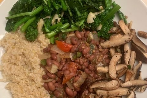 A plated meal with sautéed mushrooms, green vegetables, rice, and beans.