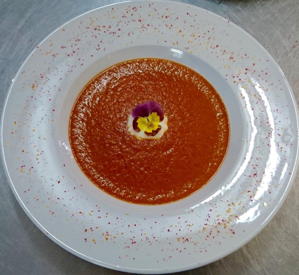 Bowl of roasted sweet pepper and Musika soup garnished with Greek yoghurt and edible flowers.