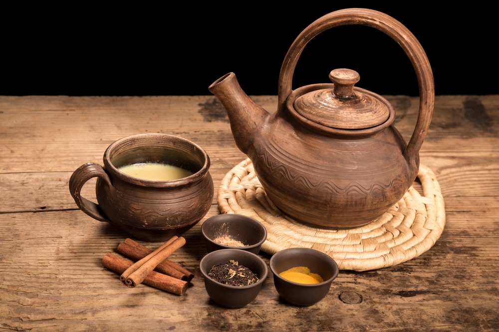 A warm masala tea setup with a teapot, cup, and array of spices on a wooden surface.