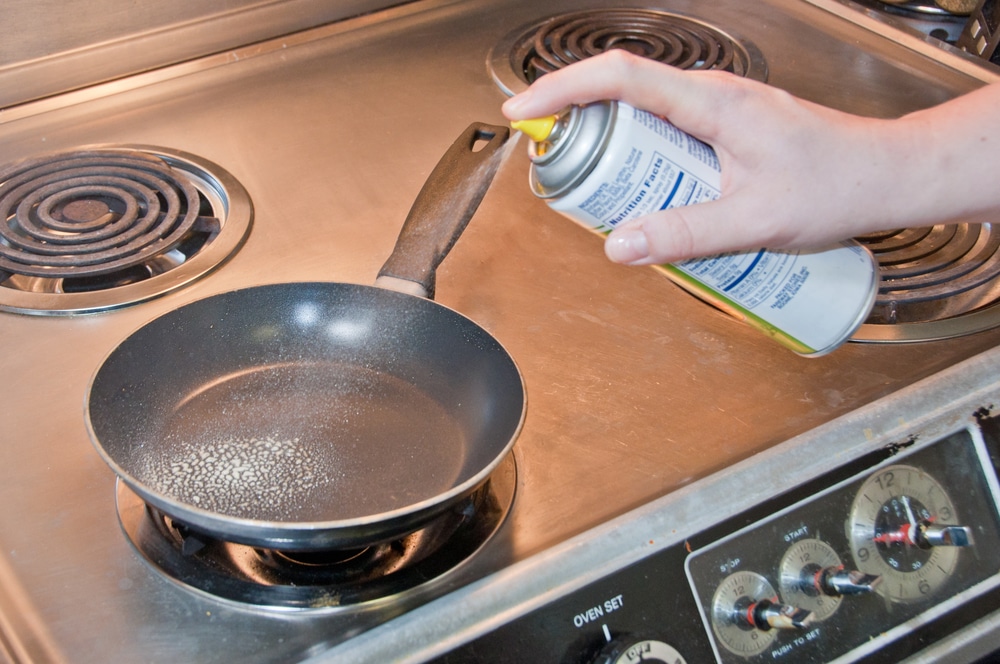 Hand spraying nonstick spray into a frying pan on an electric stove