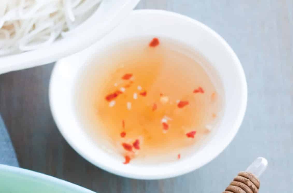 Close-up view of Nuoc Cham sauce with red chili pepper flakes floating on top.