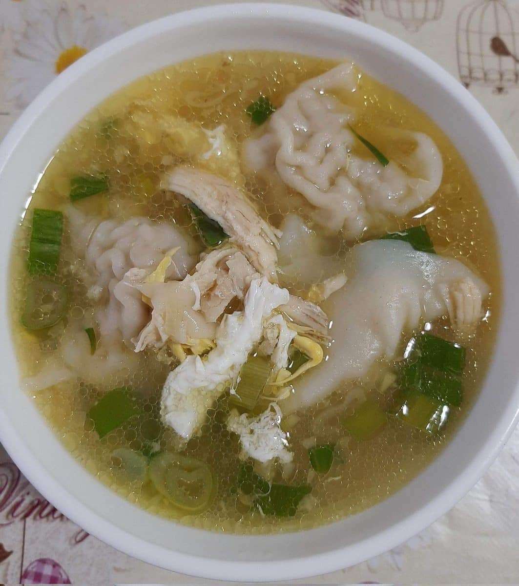 A bowl of Pancit Molo, Filipino pork dumpling chicken soup, with fresh garnish.