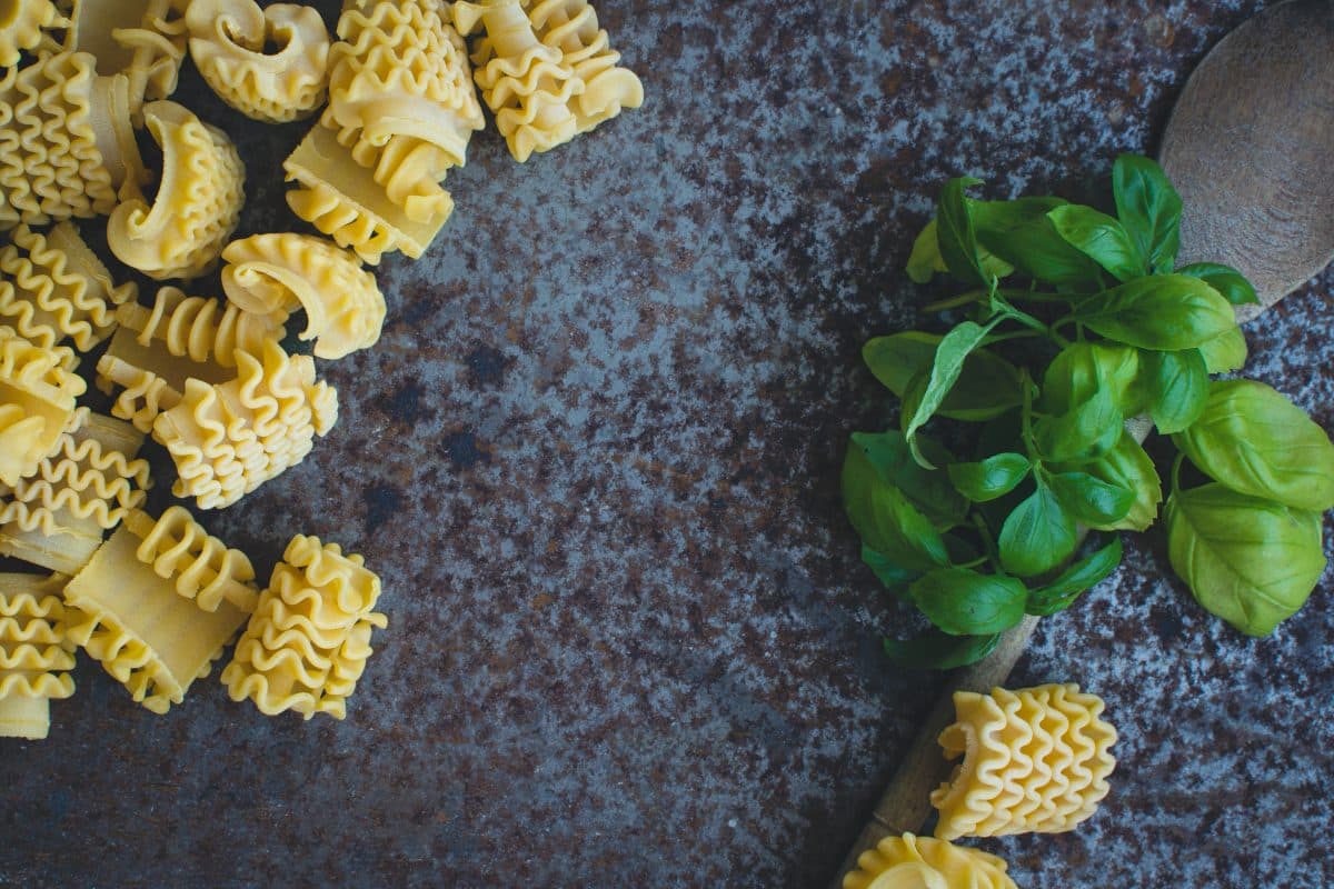 Radiatore pasta with fresh basil leaves next to a wooden spoon on a rustic surface.