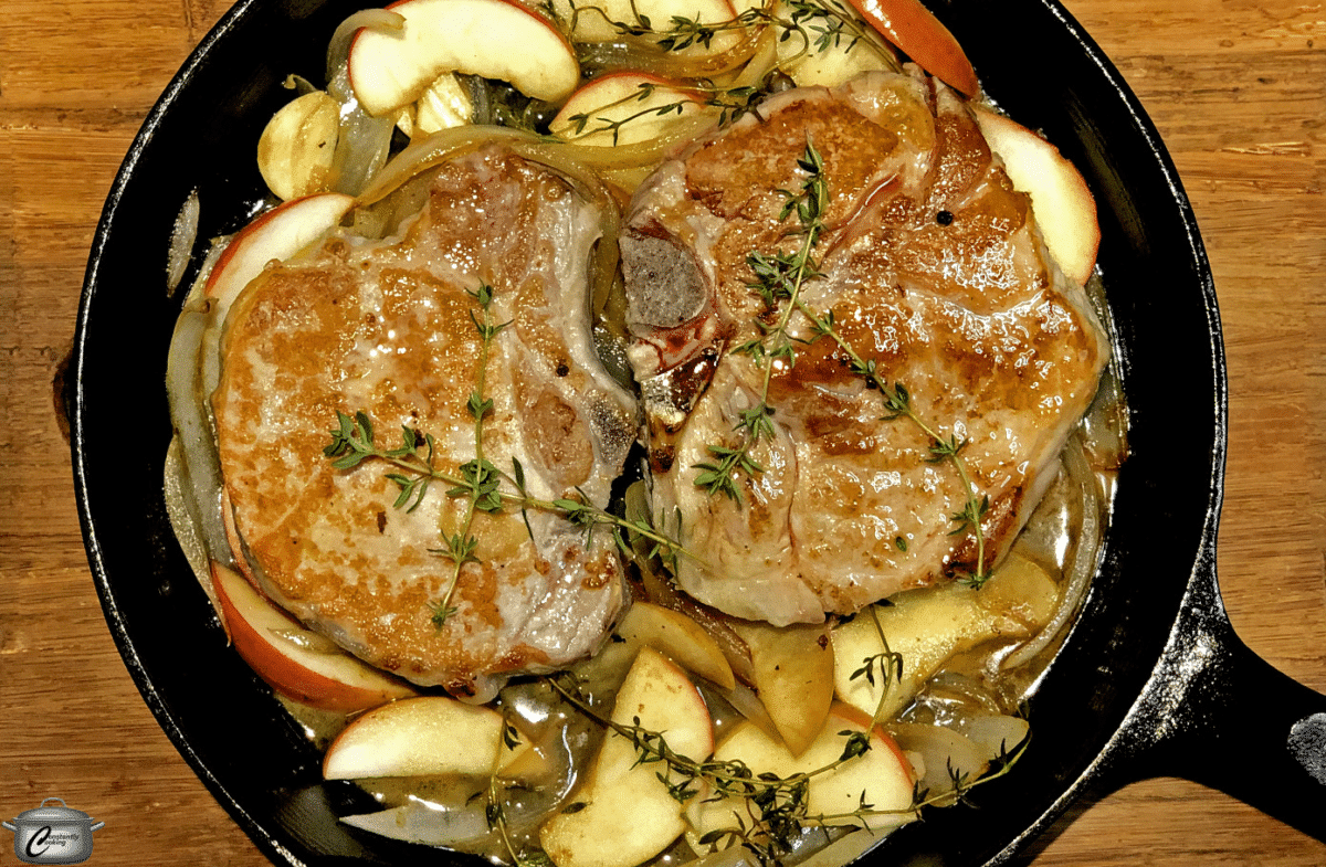 Close-up view of brined pork chops cooked with apples in a skillet.