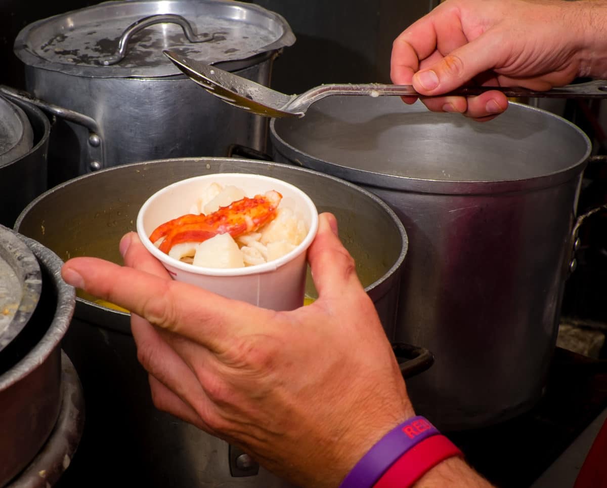 Close-up of a man's hands ladling seafood stew from a large stock pot