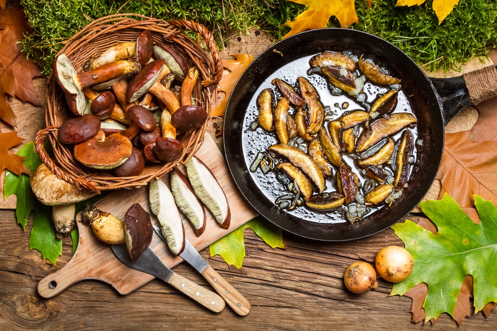Mixed raw mushrooms on a cutting board beside a skillet with sautéed mushrooms.