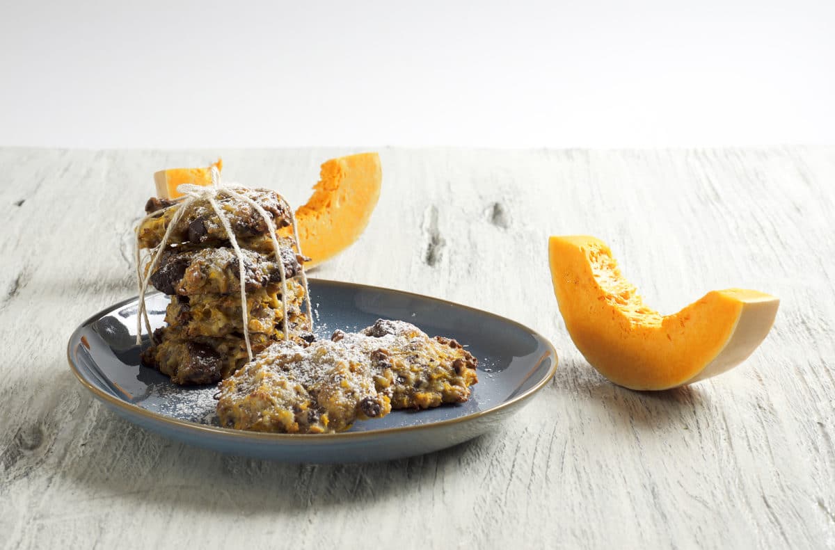 A plate of pumpkin, chocolate, and butterscotch chip cookies next to pumpkin slices.
