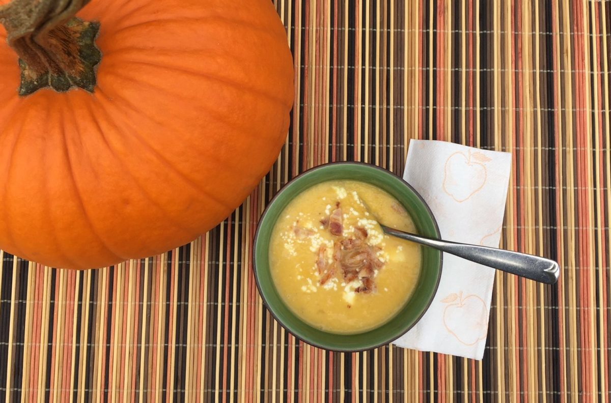 A bowl of pumpkin soup garnished with blue cheese and bacon.