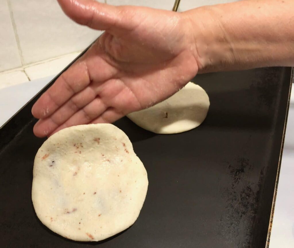 Hand placing a filled pupusa onto a grill