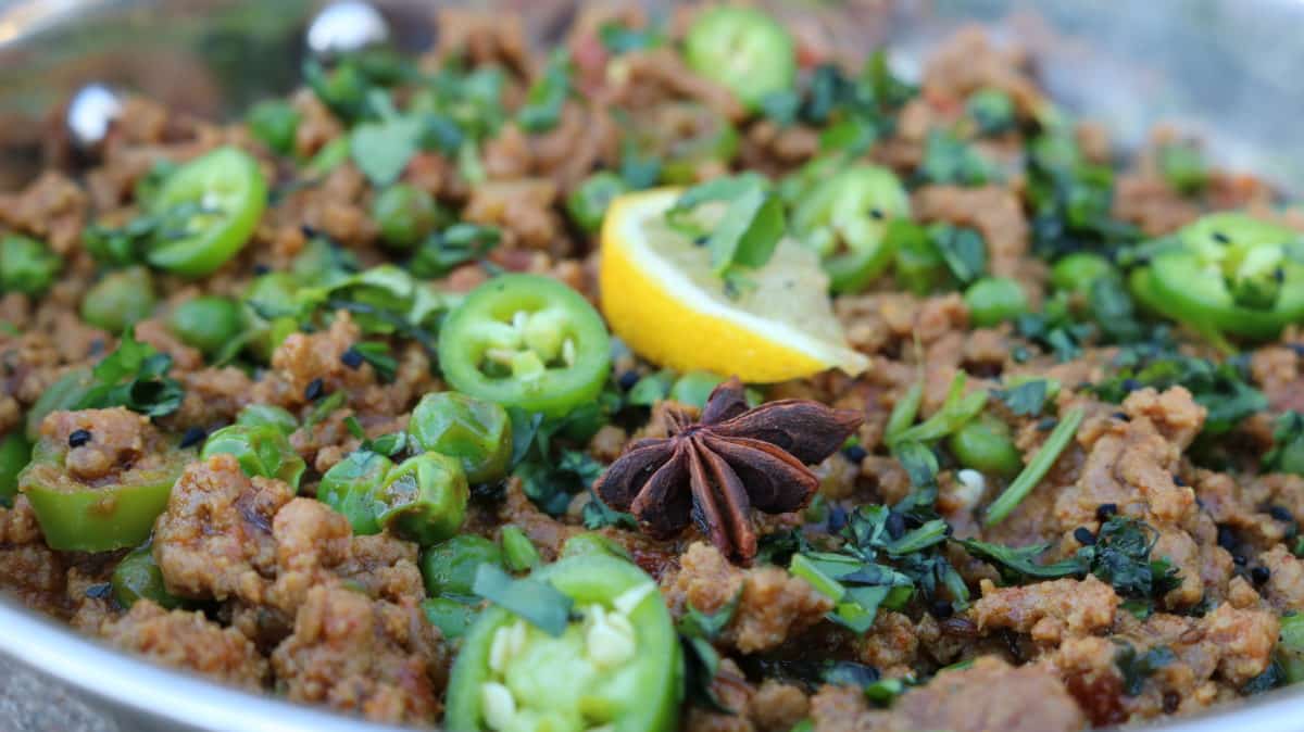 A flavorful Qeema Mutter dish garnished with green chili slices, fresh herbs, and an aromatic star anise.