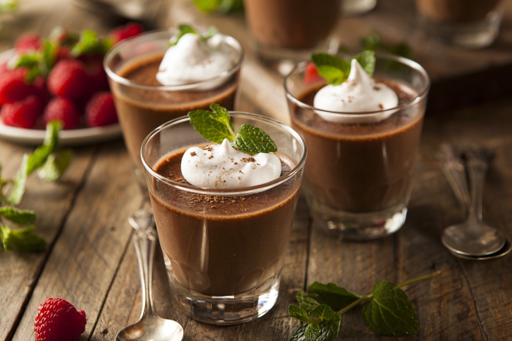 Glasses filled with dark chocolate mousse topped with whipped cream and fresh raspberries.