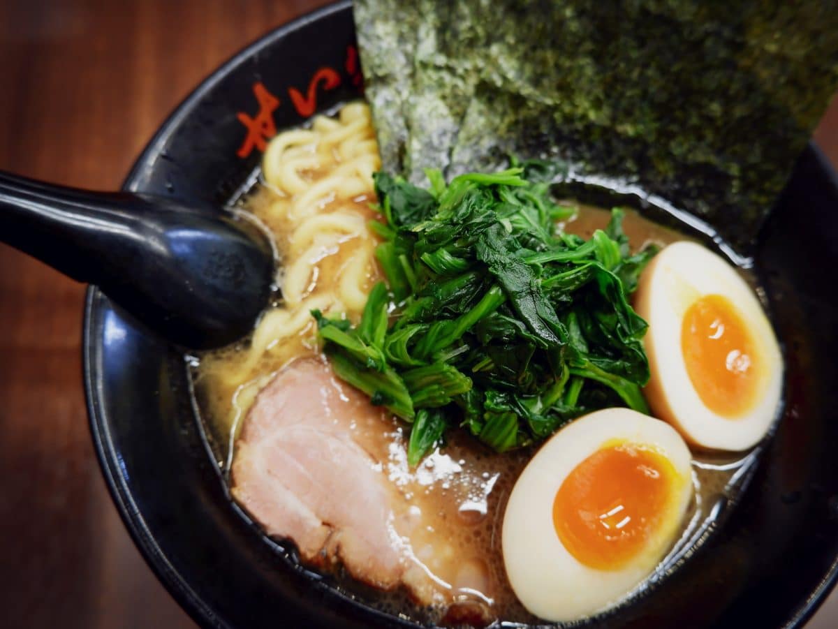 A bowl of ramen with sliced pork, spinach, seaweed, and a soft-boiled egg.