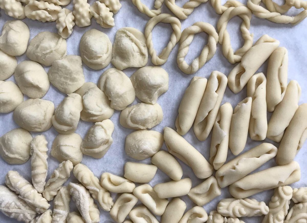 Assorted shapes of raw, hand-rolled pasta on parchment paper.