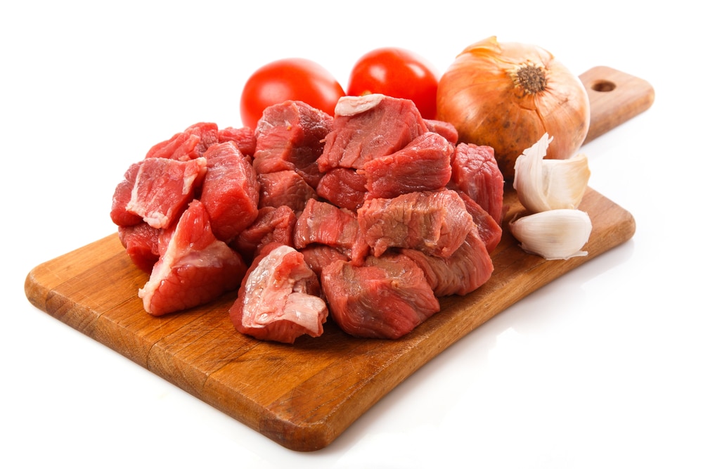 Raw red meat cubes arranged on a wooden board against a white background.