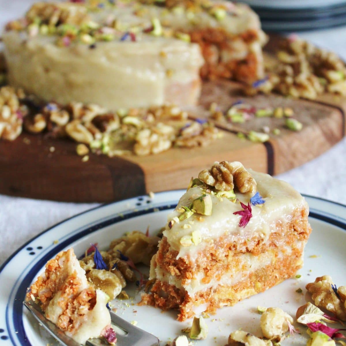 Slice of raw vegan carrot cake topped with walnuts and decorative flowers.