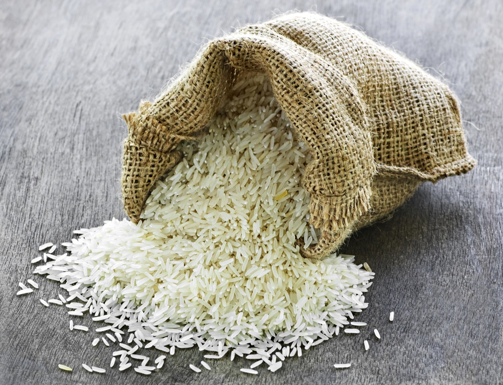 Raw long grain white rice spilling from a burlap bag.