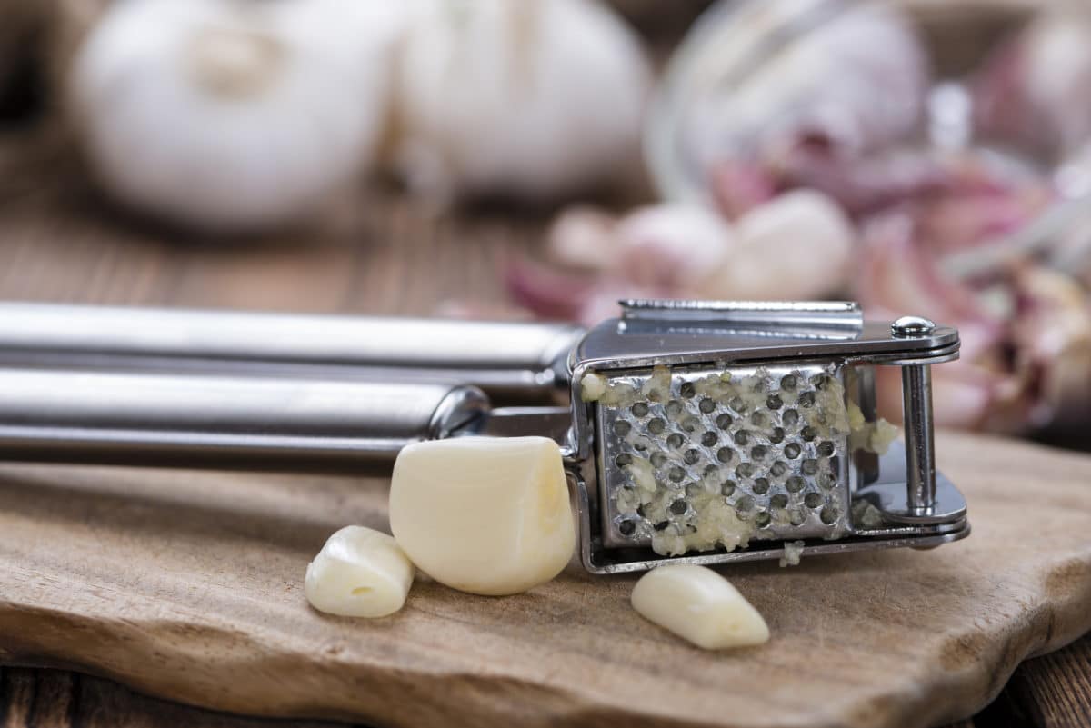 Close-up of a garlic press with fresh garlic cloves beside.