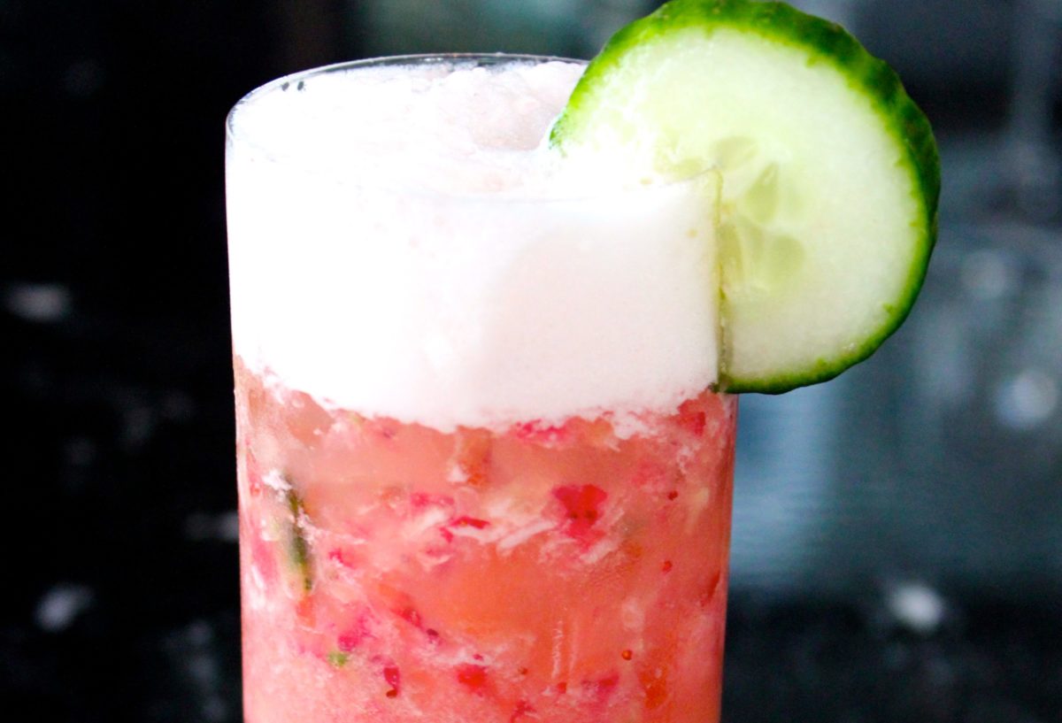 A vibrant red cocktail garnished with a cucumber slice.
