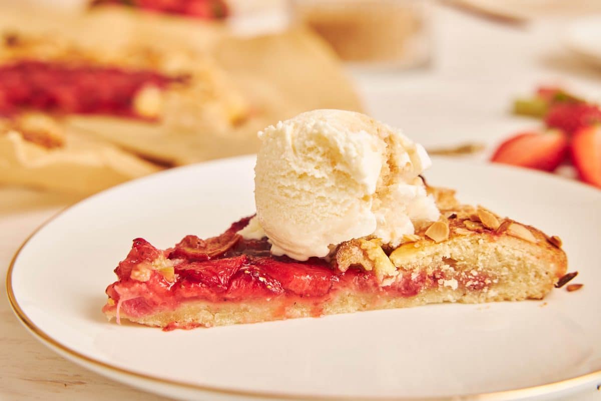 Close-up of a rhubarb and strawberry cake slice topped with a scoop of vanilla ice cream.