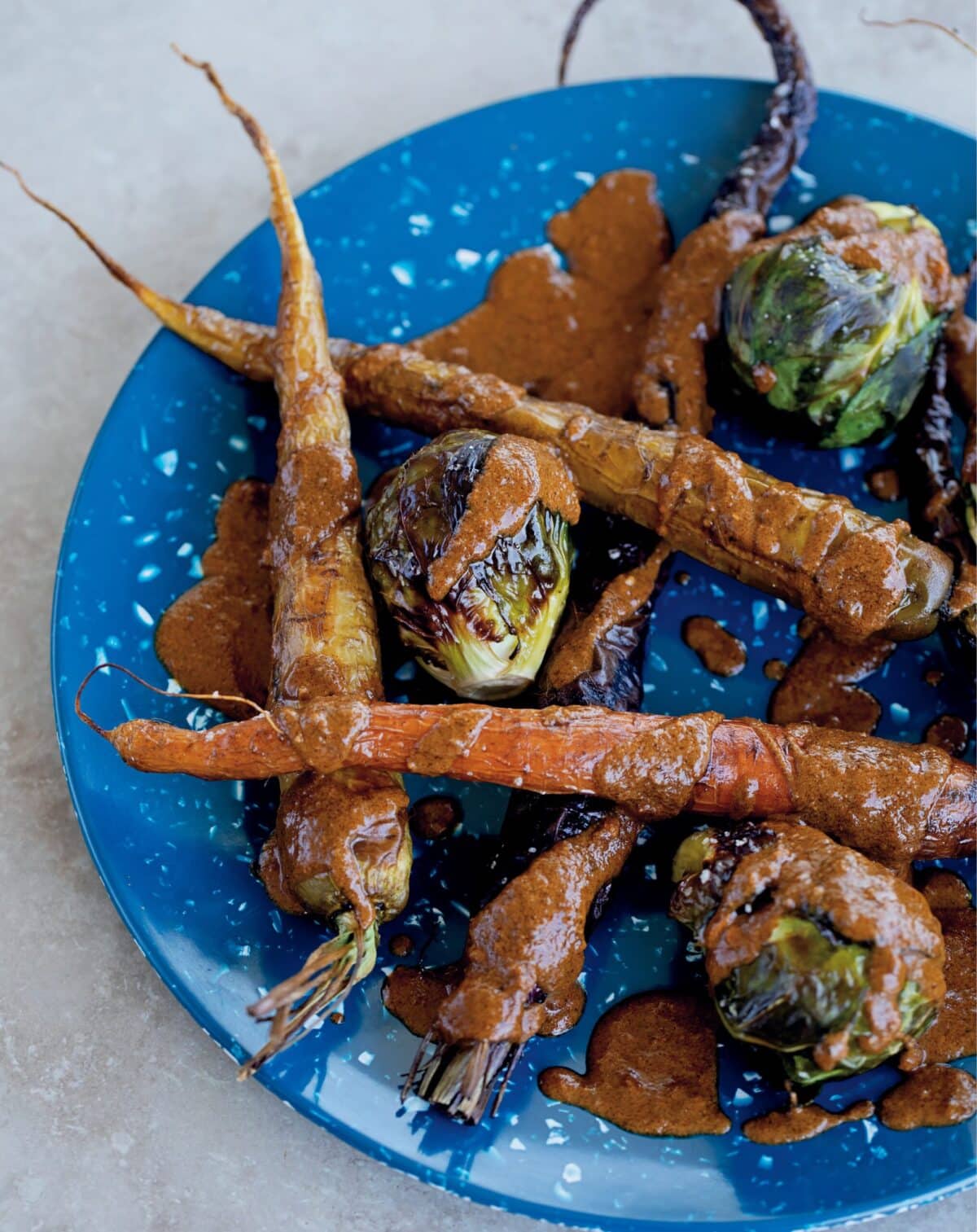Roasted brussel sprouts and carrots on a blue plate with sauce.
