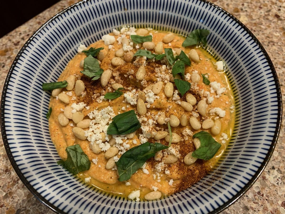Close-up of Poivronnade spread topped with pine nuts and basil leaves on a striped plate.