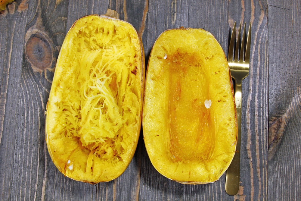 Overhead view of roasted spaghetti squash, one half scraped to display strands.