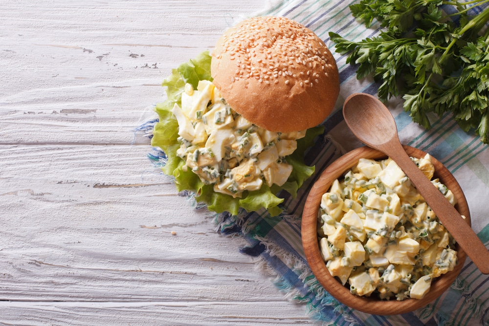 Rustic style egg salad sandwich on a wooden table, garnished with herbs. Horizontal view.