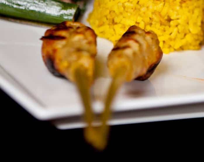 Grilled fish skewers on a plate with yellow rice.