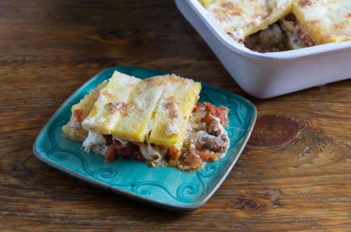 Close-up view of a slice of sausage and cheese polenta pie served on a blue plate.