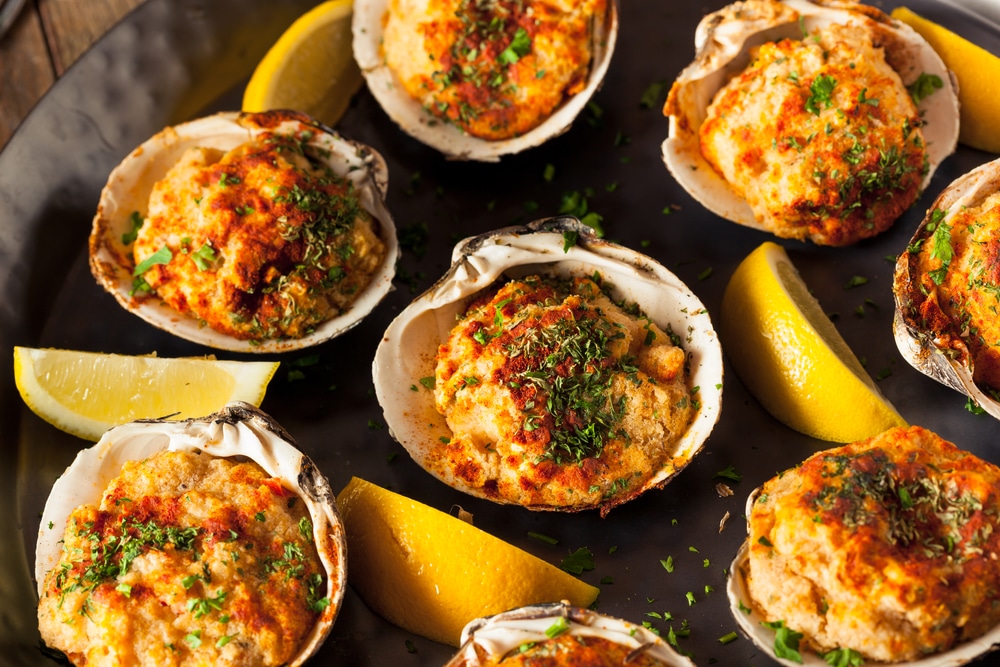 A platter of baked clams casino garnished with herbs and lemon wedges.