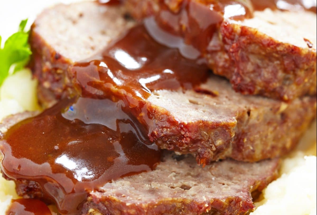 Close-up of meatloaf slices with brown sauce on creamy mashed potatoes.