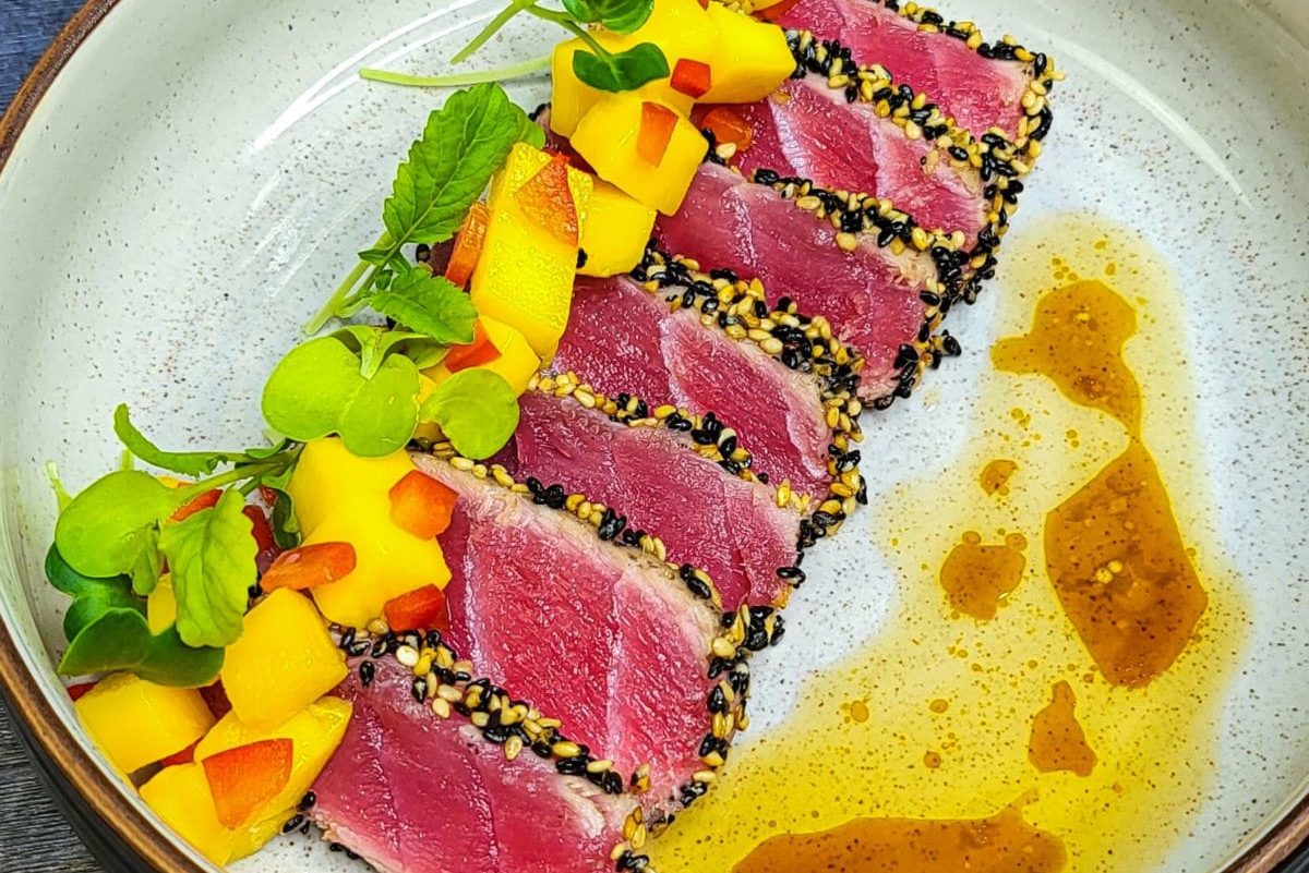Sliced seared ahi tuna garnished with mango and herbs on a plate.