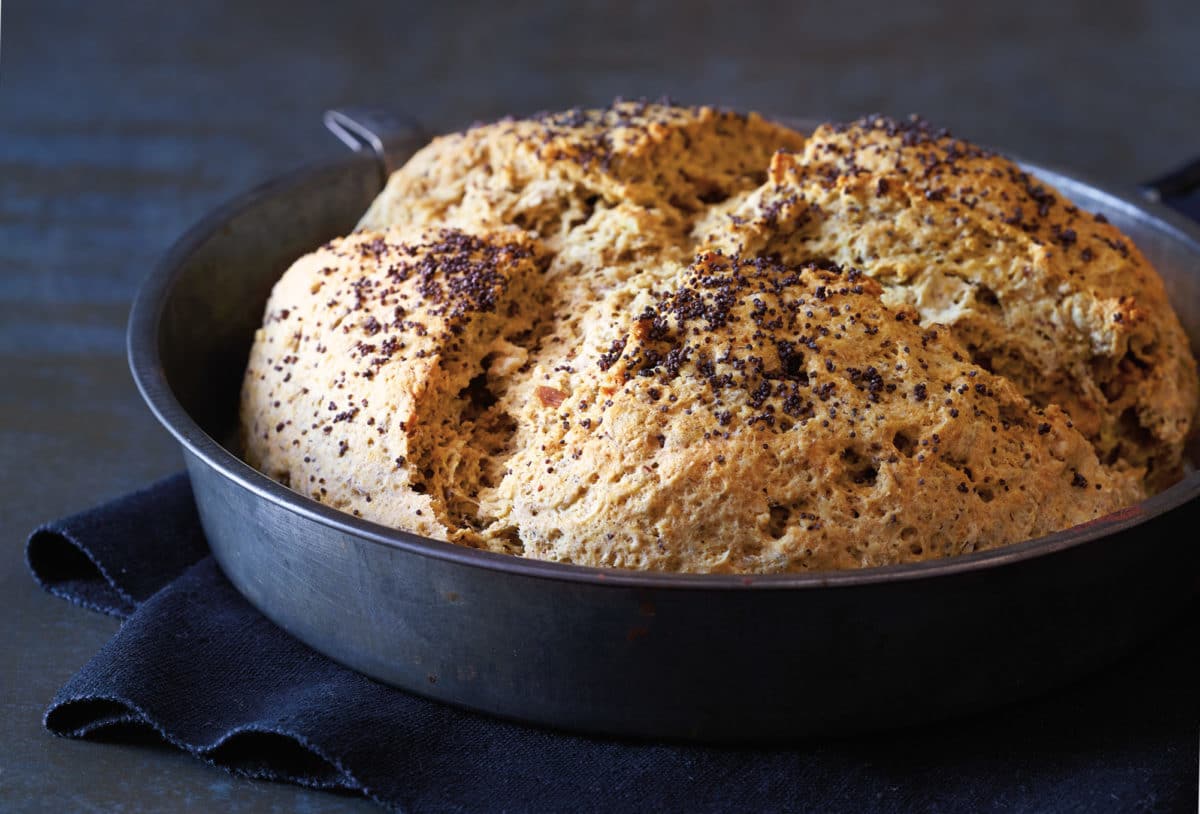 Freshly baked Seeded Irish Soda Bread with a golden-brown crust sprinkled with seeds, placed in a round pan.