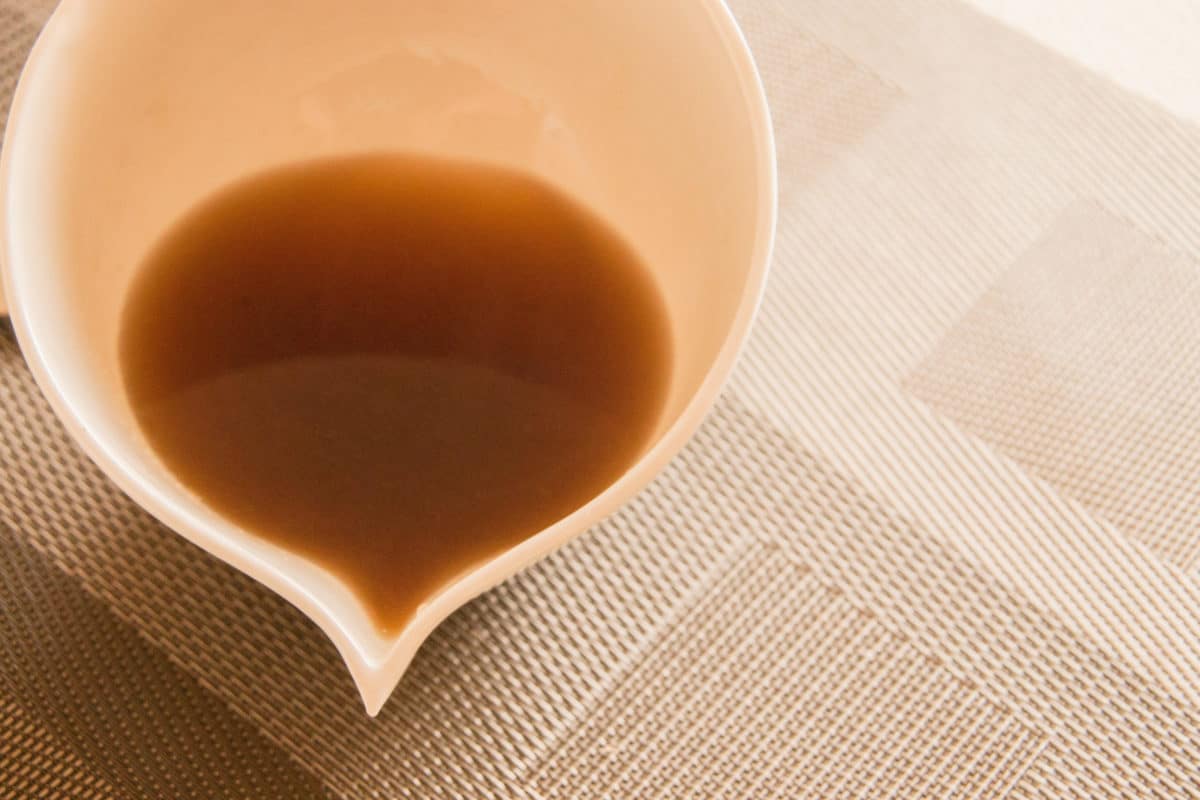 Brown syrup in a ceramic dish on a woven mat.