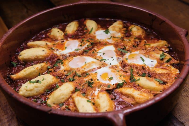 Shakshuka dish with duck eggs and sausages in a clay pot.