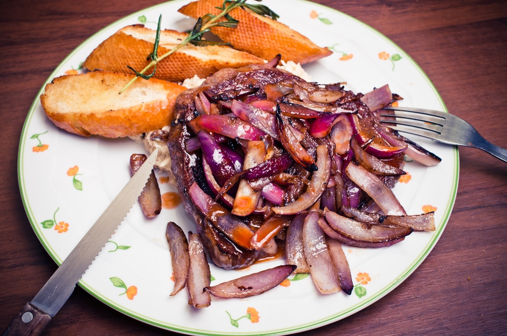Pan-seared sirloin steak accompanied by sautéed onions, mushrooms, and peppers, served with crusty bread slices.