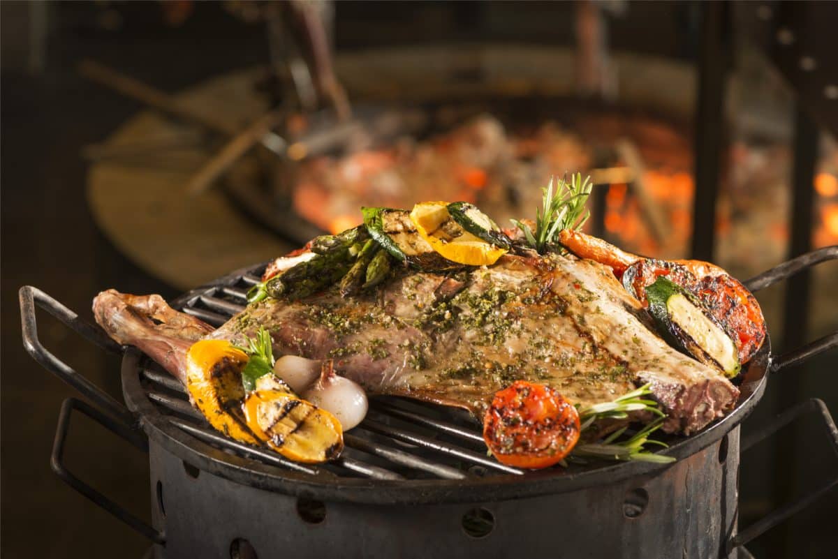 Slow-cooked roasted goat (Cabrito) garnished with assorted vegetables on a grill.