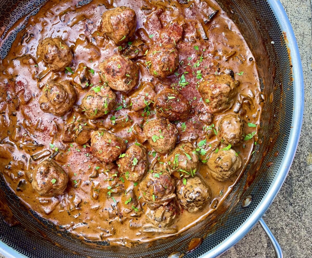 Pan of golden-brown meatballs with herbs in a rich sauce