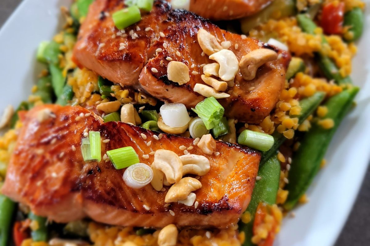 Grilled sockeye salmon served with sautéed veggies and red lentils, garnished with cashews and spring onions.