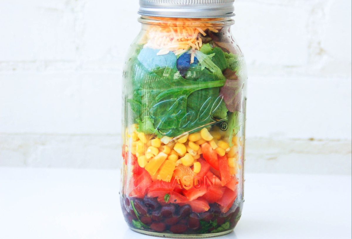 A mason jar filled with Southwestern Salad featuring green dressing, tomatoes, and avocado.