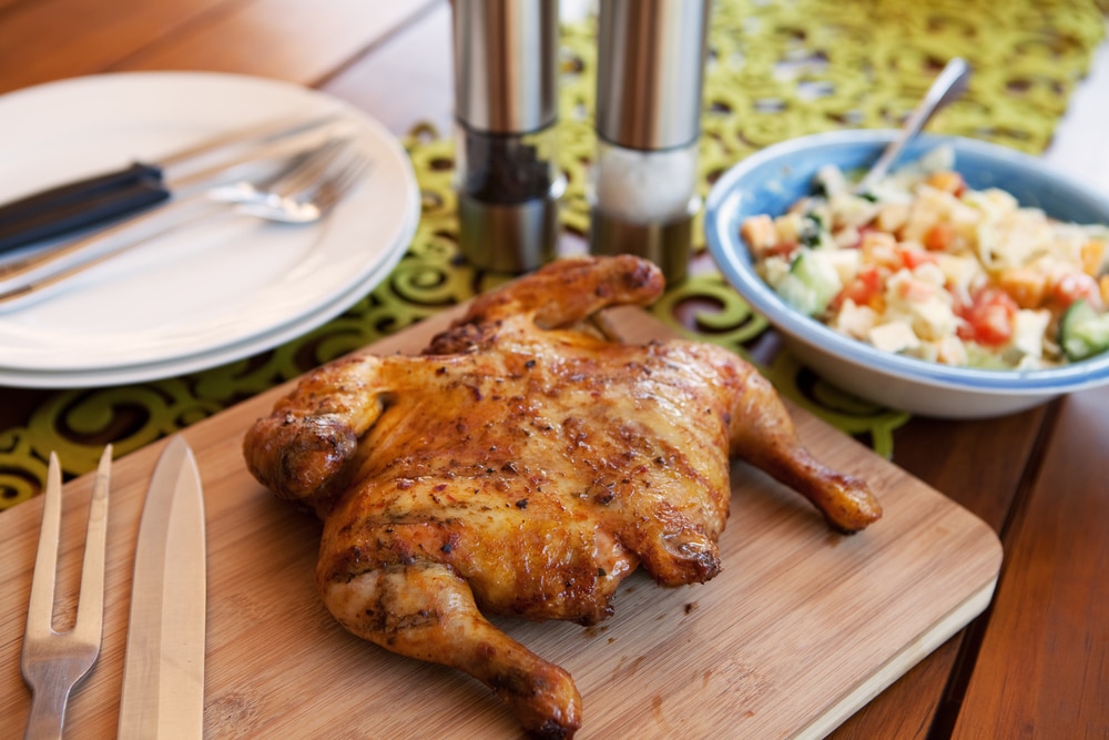 Whole roasted chicken on wooden board accompanied by a fresh salad.