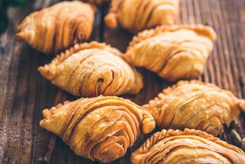 Golden brown spiral curry puffs on a wooden surface.