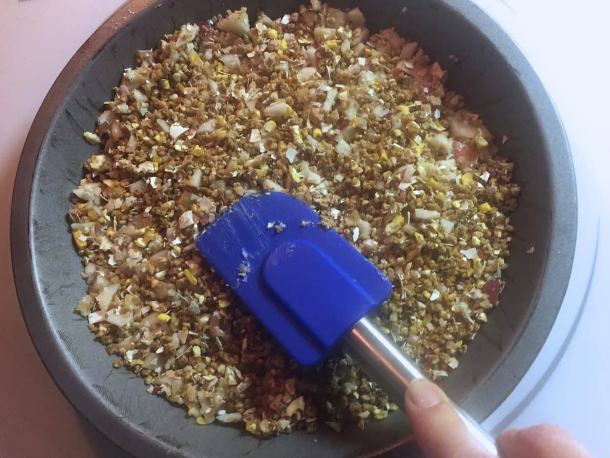 Hand using a spatula to spread chicken treat mix in a round pan.